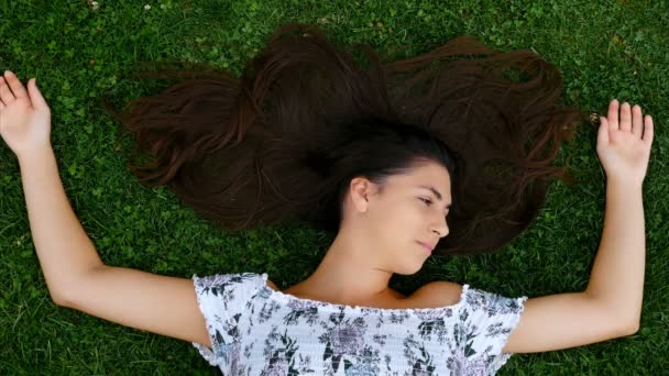 Mooie gelukkig lachend meisje liggend op het gras met het verspreiden van haar, 4k - Video