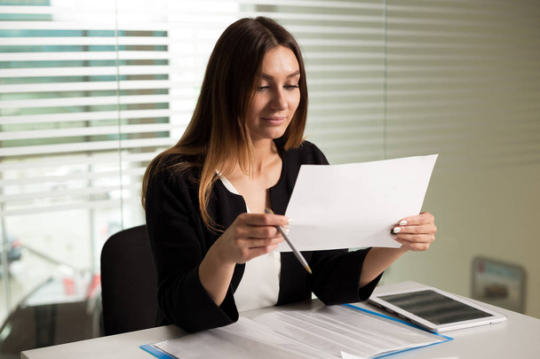 young businesswoman girl with glasses in casual wear sitting at the table carefully look at the documents  - Photo, Image