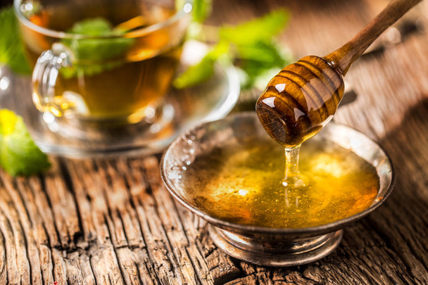 Honey. Honey and honey dipper on rustic oak table. Hot herb tea in the background - Foto, Imagen