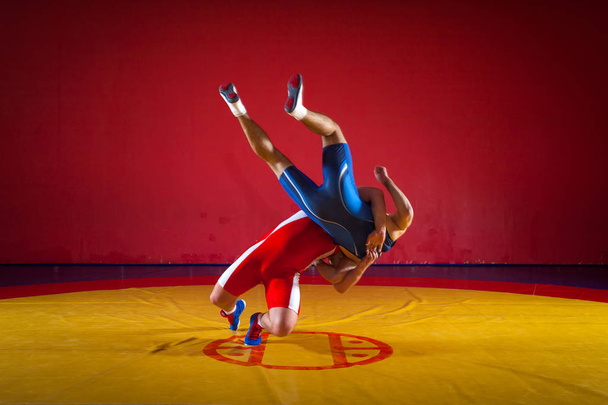Zwei starke Wrestler in blauen und roten Wrestlingstrumpfhosen ringen auf einem gelben Wrestlingteppich in der Turnhalle. Junger Mann macht Rangelei. - Foto, Bild