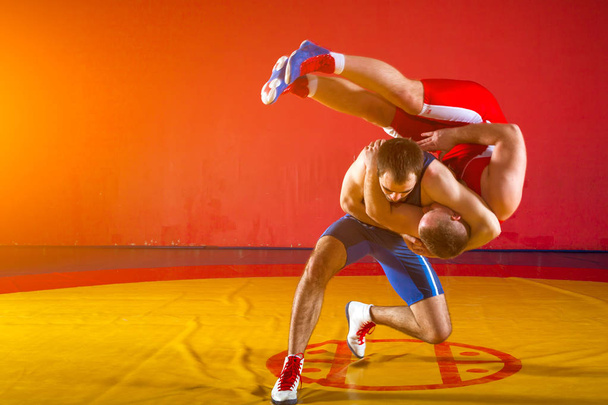 Dwóch grecko-rzymskich zapaśników w czerwonym i niebieskim wrestlingu na żółtym dywanie zapasowym w siłowni - Zdjęcie, obraz