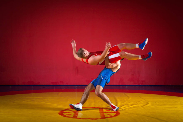 Dwóch grecko-rzymskich zapaśników w czerwonym i niebieskim wrestlingu na żółtym dywanie zapasowym w siłowni - Zdjęcie, obraz