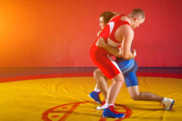 Два сильных борца в синих и красных борцовских трико борются и борются на желтом борцовском ковре в тренажерном зале
.  - Фото, изображение