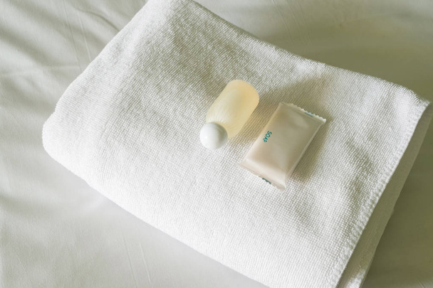 Φθηνό ξενοδοχείο κρεβάτι με σαμπουάν και σαπούνι μπουκάλι σε λευκή πετσέτα. - Φωτογραφία, εικόνα