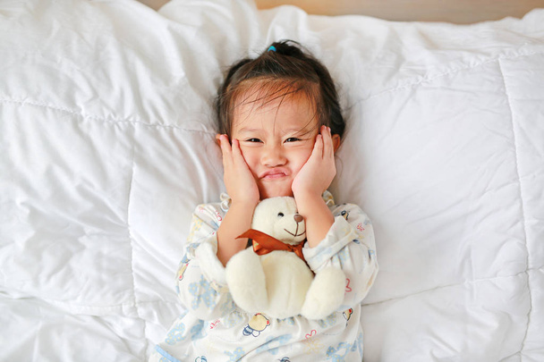 Funny face asian little girl with teddy bear lying on bed - 写真・画像