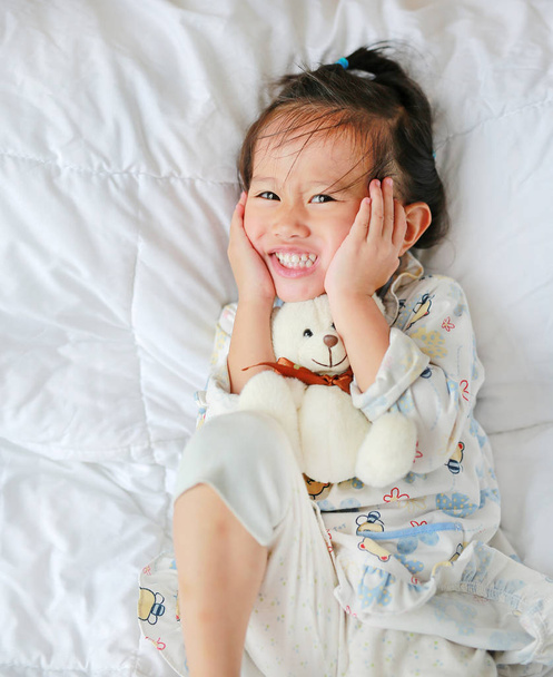 Funny face asian little girl with teddy bear lying on bed - Fotó, kép