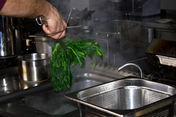 A szakács főzött zöld meleg spenót egy serpenyőben, a veszi a - Fotó, kép
