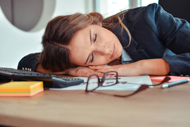 Overwerkt en moe jonge vrouw slapen op Bureau - Foto, afbeelding