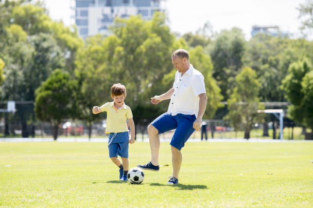 fiatal, boldog apa és izgatott kis 7 vagy 8 éves fia játszik együtt Labdarúgás soccer city park kerti fut a fű rúgja a labdát - Fotó, kép