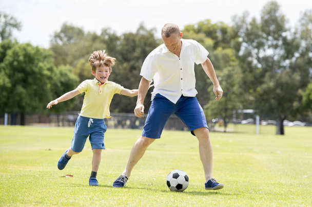 молодой счастливый отец и взволнованный маленький 7 или 8-летний сын играют вместе футбол в саду городского парка работает на траве ногами мяч
 - Фото, изображение