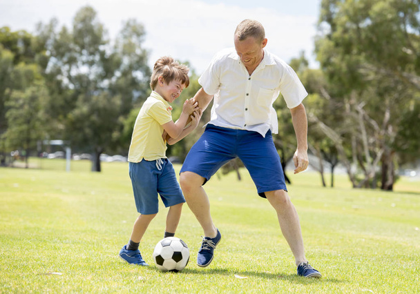 joven feliz padre y emocionado poco 7 u 8 años de edad hijo jugando juntos fútbol en el jardín del parque de la ciudad corriendo sobre la hierba pateando la pelota
 - Foto, Imagen