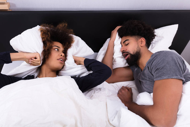 Elevated View Of Young Woman Covering Her Ears With Pillow While Man Snoring In Bed - Photo, Image