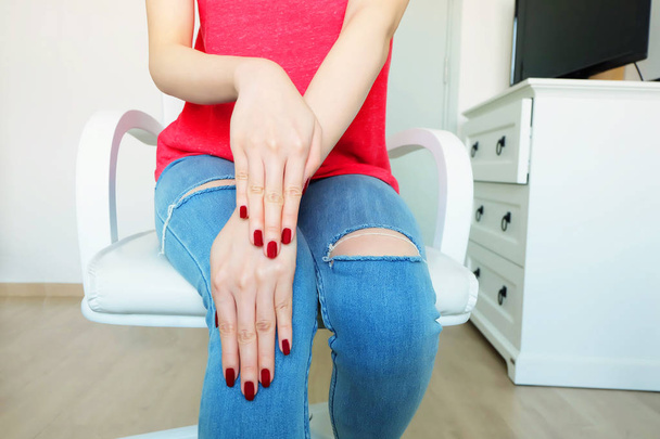 Close Up Red Nails Manicure Cosmetics. Beautiful Woman with Red Nail Polish and Red Shirt Sitting on a White Chair Background Great for Any Use. - Foto, imagen