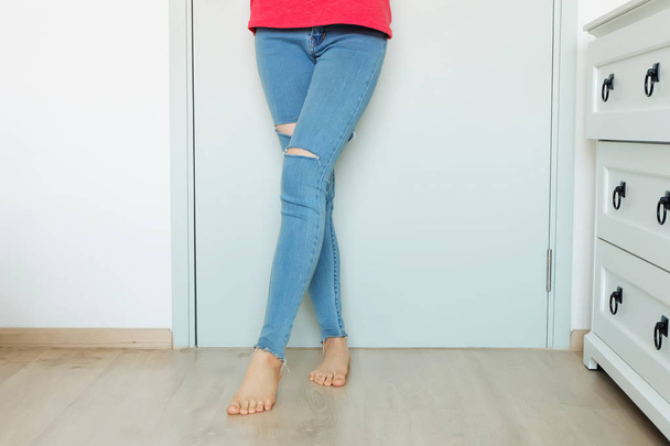 Close-up van rode nagels Manicure. Mooie vrouw portret met Blue Jeans ontbreken knie permanent op witte kamer achtergrond grote voor elk gebruik. - Foto, afbeelding