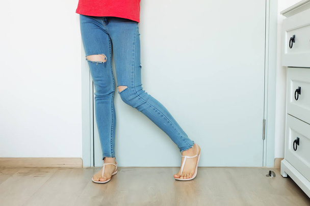 Zblízka červené nehty manikúra. Krásná žena portrét s modré džíny nedostatek kolen stojící na pozadí velké bílé místnosti pro jakékoliv použití. - Fotografie, Obrázek