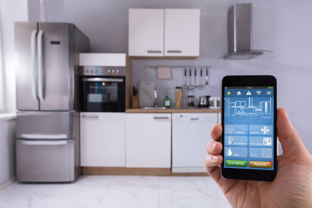 Close-up Of A Person's Hand Using Smart Home System On Mobilephone In Kitchen - Foto, Imagen