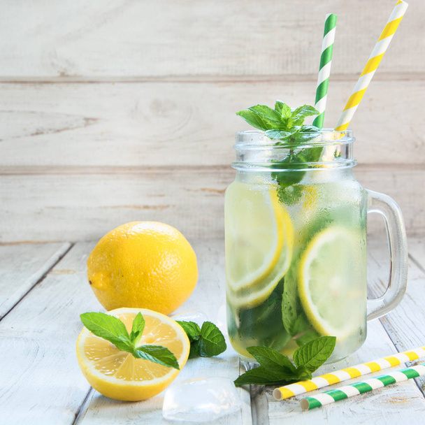Summer refreshing detox cocktail. Water with lemon, mint and ice in mason jar on white wooden board. Rustic style. - 写真・画像