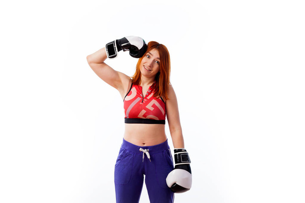 jeune femme rousse en tenue de sport et gants de boxe noir et blanc sourit et se frappe sur la boîte à tête sur fond blanc isolé
... - Photo, image
