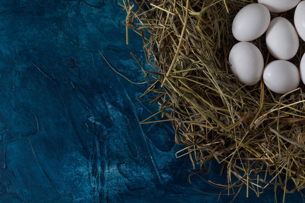 Huevos de pollo en un nido cubierto con un paño blanco en una espalda azul
 - Foto, Imagen