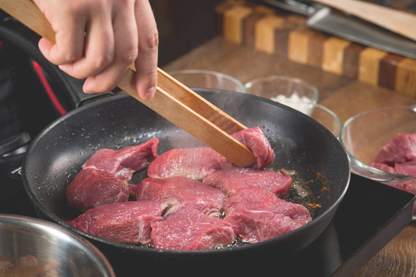 Chef cooks raw meat in a frying pan for cooking a recipe with fried meat - Fotografie, Obrázek