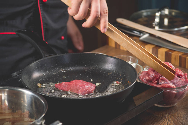 Chef cooks raw meat in a frying pan for cooking a recipe with fried meat - Fotografie, Obrázek