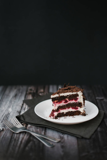 Kawałek ciasto czekoladowe z wiśniami i jogurt napełniania serwowane na białe płytki z serwetki na tle ciemnego drewniany stół - Zdjęcie, obraz
