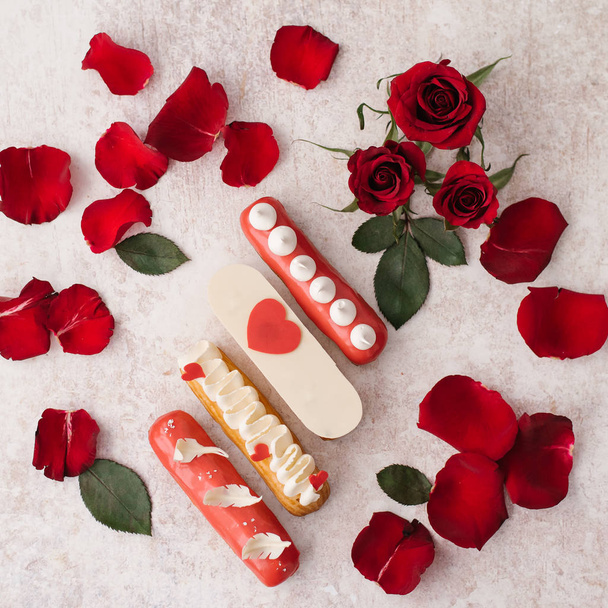 View of decorated eclairs, red petals and red roses on beige background - Fotografie, Obrázek