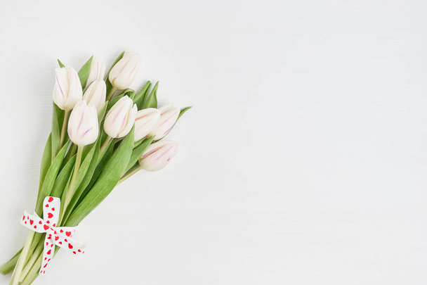 Λευκές τουλίπες μπουκέτο διακοσμημένα με καρδιές κορδέλα σε άσπρο φόντο ξύλινη. Αντιγράψτε το χώρο, το top view. Ημέρα του Αγίου Βαλεντίνου έννοια - Φωτογραφία, εικόνα