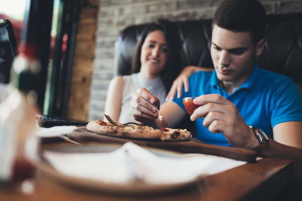 Atraktivní a šťastný mladý pár se dobře baví v kavárně restaurace. Usmívají se a jedí pizzu - Fotografie, Obrázek