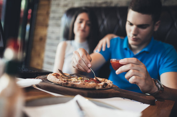 カフェレストランで楽しい時間を過ごしている魅力的で幸せな若いカップル。彼らは笑ってピザを食べている - 写真・画像