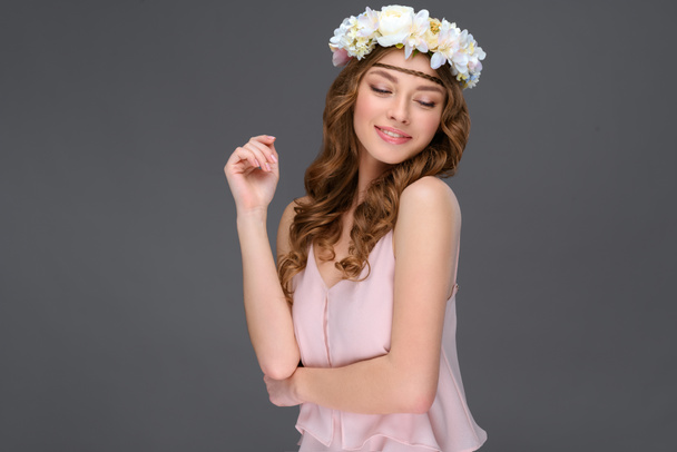 smiling young woman with curly hair in white floral wreath isolated on grey - Foto, immagini
