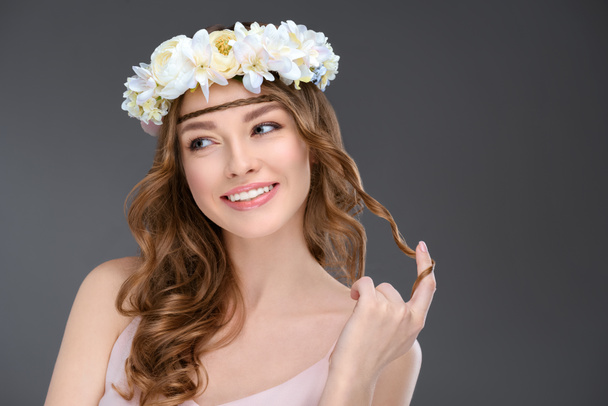playful young woman with curly hair in floral wreath isolated on grey - Fotó, kép