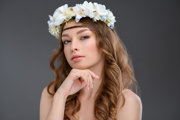 attractive young woman with curly hair in floral wreath isolated on grey - Zdjęcie, obraz