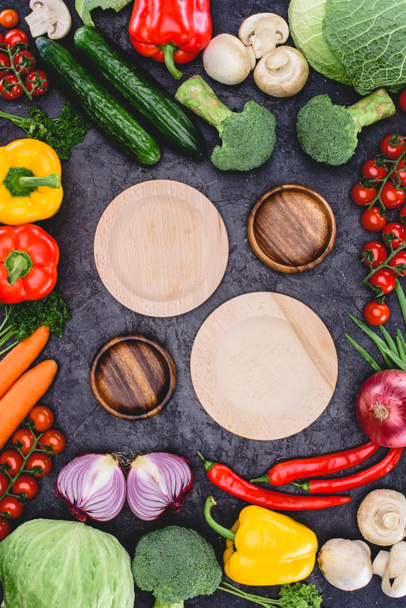 top view of empty wooden plates and fresh raw organic vegetables on black - Photo, Image