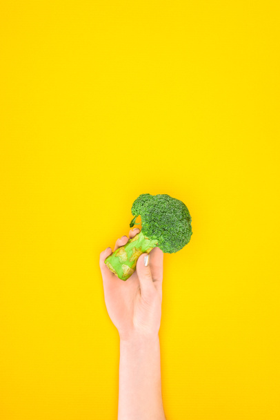 tiro recortado de la persona que sostiene el brócoli orgánico verde fresco aislado en amarillo
 - Foto, Imagen