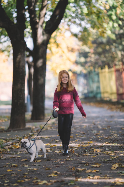 People and dogs outdoors. Beautiful and happy redhead girl enjoying in autumn park walking with her adorable French bulldog - Foto, immagini