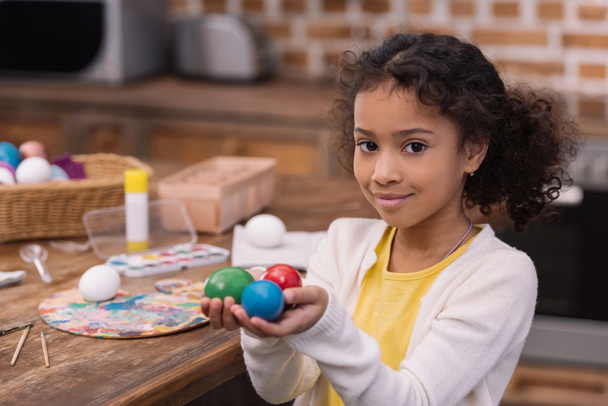 Αφρικανική αμερικανική παιδί κρατώντας βαμμένα πασχαλινά αυγά στα χέρια και βλέπουν τα φωτογραφικών μηχανών - Φωτογραφία, εικόνα