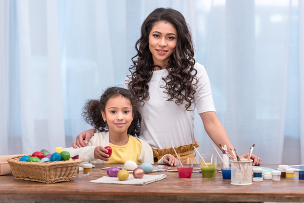 african american mother and daughter standing near table with easter eggs and looking at camera - Zdjęcie, obraz