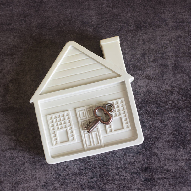 Μικρό λευκό σπίτι και ένα διακοσμητικό κλειδί σε σκούρο φόντο. - Φωτογραφία, εικόνα