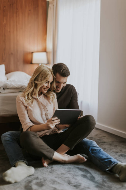 Αγάπη ζευγάρι κάθεται στο πάτωμα στην κρεβατοκάμαρα και χρησιμοποιώντας ψηφιακό tablet - Φωτογραφία, εικόνα