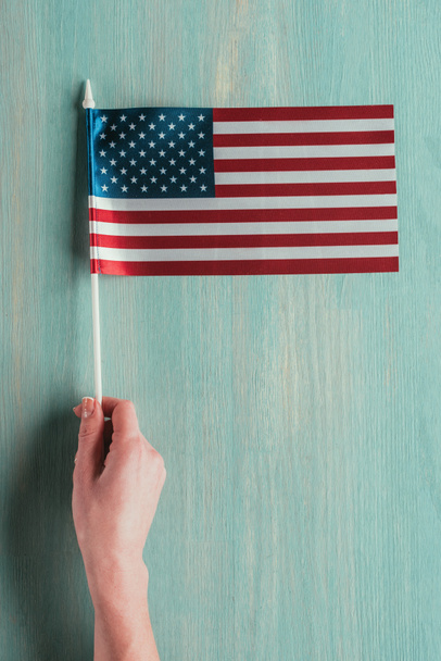 partial view of woman holding american flag in hand on blue wooden tabletop, presidents day concept - Fotó, kép
