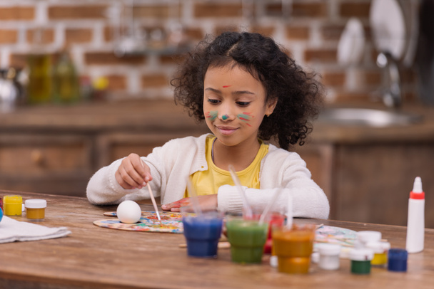 african american kid painting easter egg in kitchen - Foto, Imagen