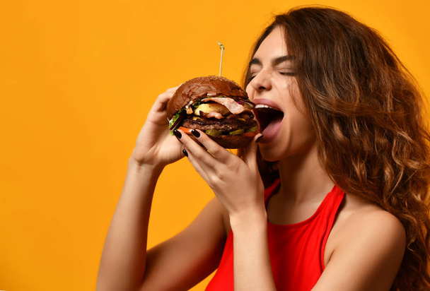 Kadın sarı arka plan üzerinde aç ağız sandviçle hamburger yemek - Fotoğraf, Görsel