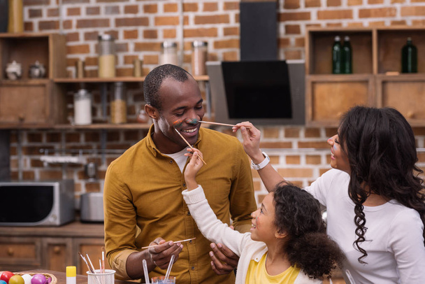 happy african american mother and daughter painting father face with paints, easter concept - Photo, Image