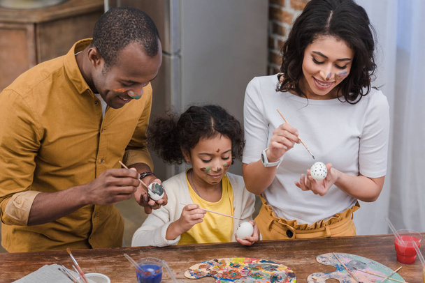 felizes pais afro-americanos e filha pintando ovos de Páscoa
 - Foto, Imagem