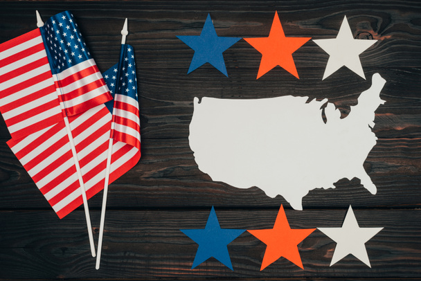 bovenaanzicht van ingerichte Amerikaanse vlaggen, stuk van kaart gemaakt van papier en sterren op houten oppervlak, voorzitters dag viering concept - Foto, afbeelding
