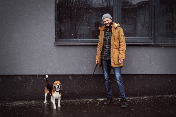 Guapo joven hipster paseando a su perro al aire libre en día nevado
 - Foto, imagen