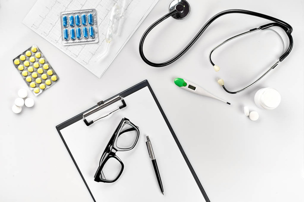 Conjunto de negocios para hospital: pastillas, estetoscopio, equipo médico, cuaderno con bolígrafo y gafas sobre fondo blanco. Médicos modernos sobre la mesa
. - Foto, imagen