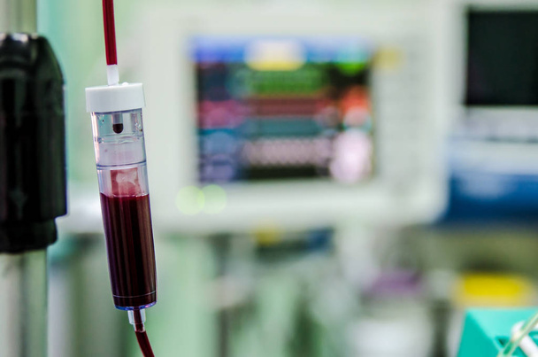 ein Tropfer mit Blut im Operationssaal auf dem Hintergrund des Monitors mit Indikatoren für das Leben des Patienten. - Foto, Bild