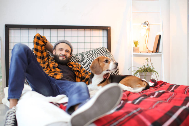 Handsome young hipster with his dog resting on bed at home - Φωτογραφία, εικόνα
